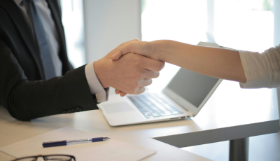 Close up of people shaking hands with laptop in background