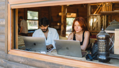 Two people on laptops through window