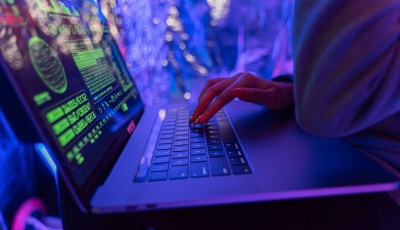 Close-up of hands typing on a laptop displaying cybersecurity graphics, illuminated by purple light.